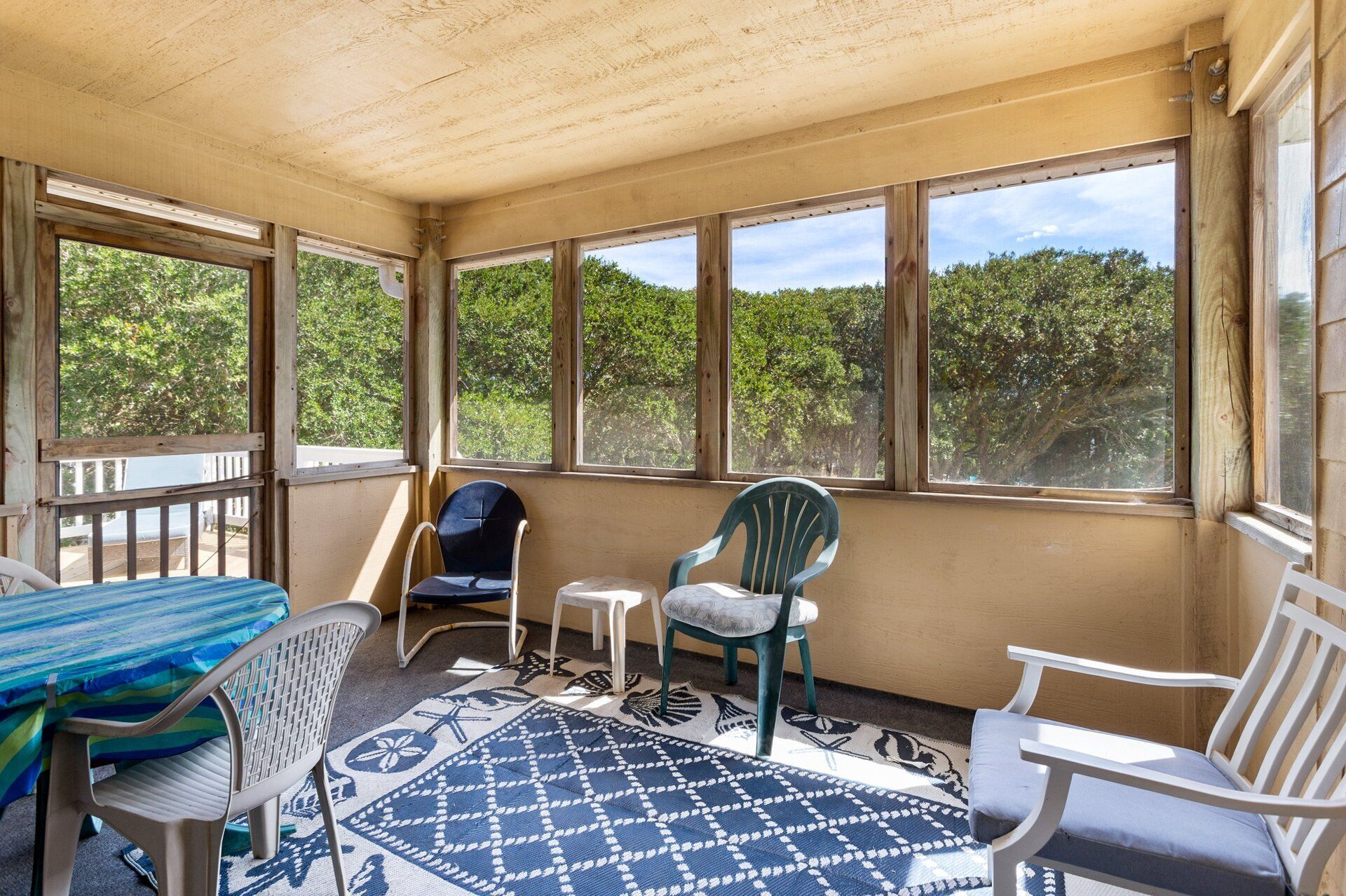 A sunroom with large windows, a table, chairs, and a patterned rug.