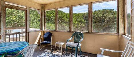 A sunroom with large windows, a table, chairs, and a patterned rug.