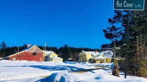 Une enseigne de l’auberge Red Clover Inn, une grange rouge et une maison jaune, le tout dans un paysage enneigé.