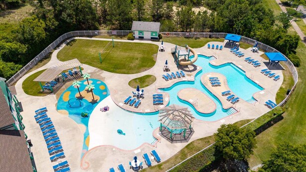 Vue aérienne d’un complexe hôtelier doté d’une grande piscine, de chaises longues, d’un toboggan aquatique et d’un pavillon.