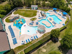 An aerial view of a resort with a large pool, sun loungers, a water slide, and a pavilion. - Fun Family Getaway | Pool, Playground & Beach Close (Kill Devil Hills)