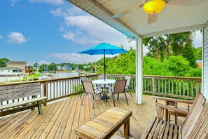 Une terrasse en bois avec une table et des chaises, un parasol bleu et une vue sur un lac où naviguent des bateaux.