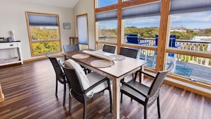 A dining area with a wooden table and chairs, large windows with blinds, and a view of a deck and landscape. - Denna's Favorite Place: Golf Views, Walk to Beach (Kitty Hawk)