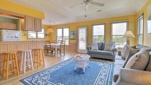 A bright living room with a grey sofa, wooden dining table, and yellow walls. - 6140 Spindrift * On the Golf Course (Nags Head)