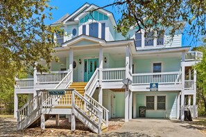 A two-story house with a porch, a staircase, and a sign that reads "Olive The Beach".