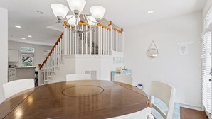 Een eetruimte met een ronde houten tafel, witte stoelen, een kroonluchter en een trap met witte leuningen.