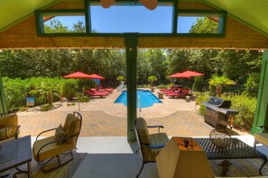 Un espace extérieur avec piscine, comprenant des chaises longues et des parasols, un barbecue et une vue sur la piscine depuis un patio couvert.