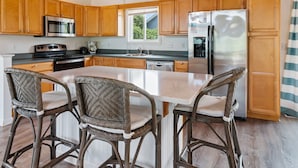 Une cuisine moderne dotée de meubles en bois, d’appareils électroménagers en acier inoxydable et d’un îlot central agrémenté de tabourets de bar.