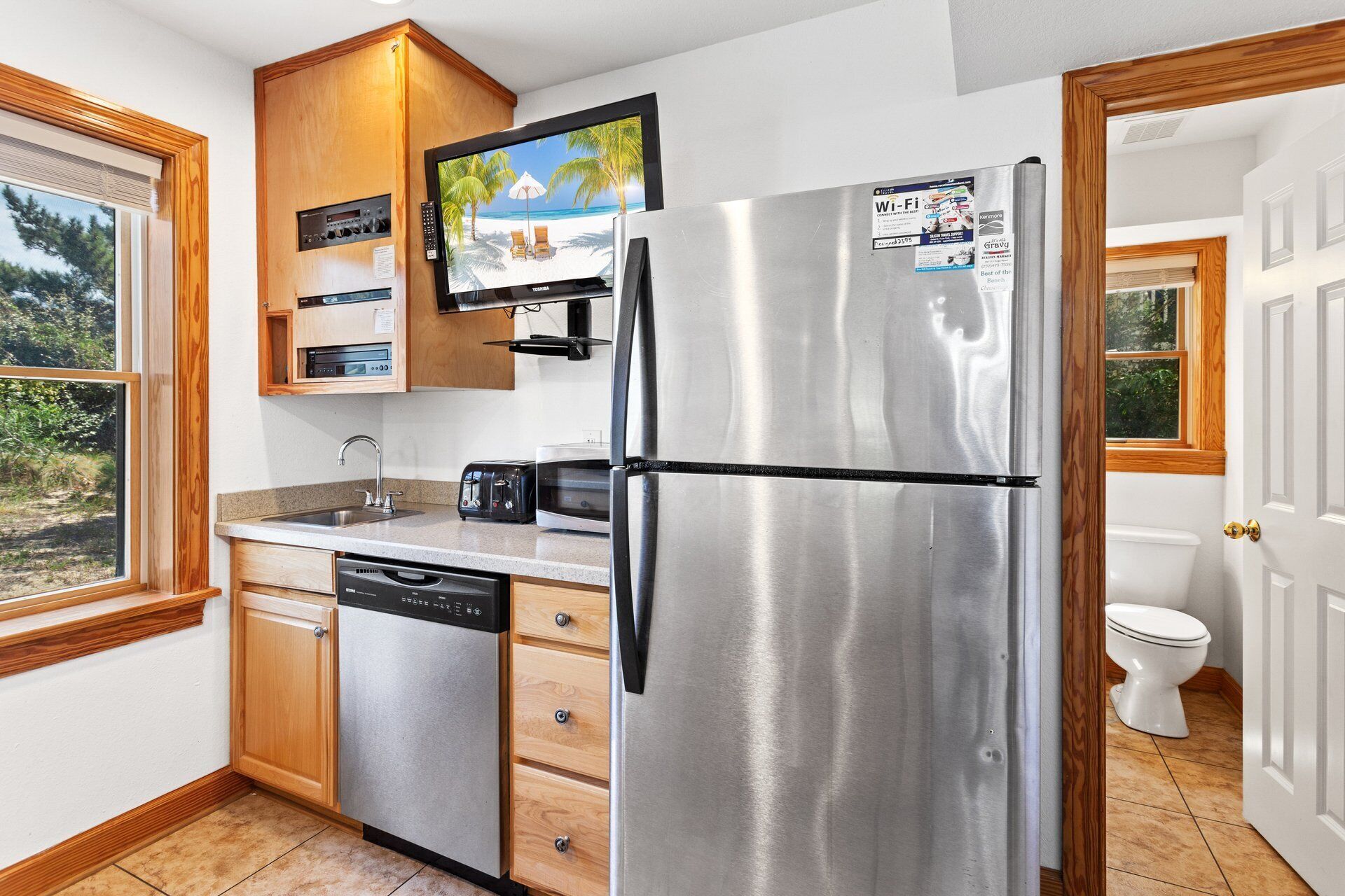 A compact kitchen with a stainless steel refrigerator, a built-in oven, a microwave, and a toaster.
