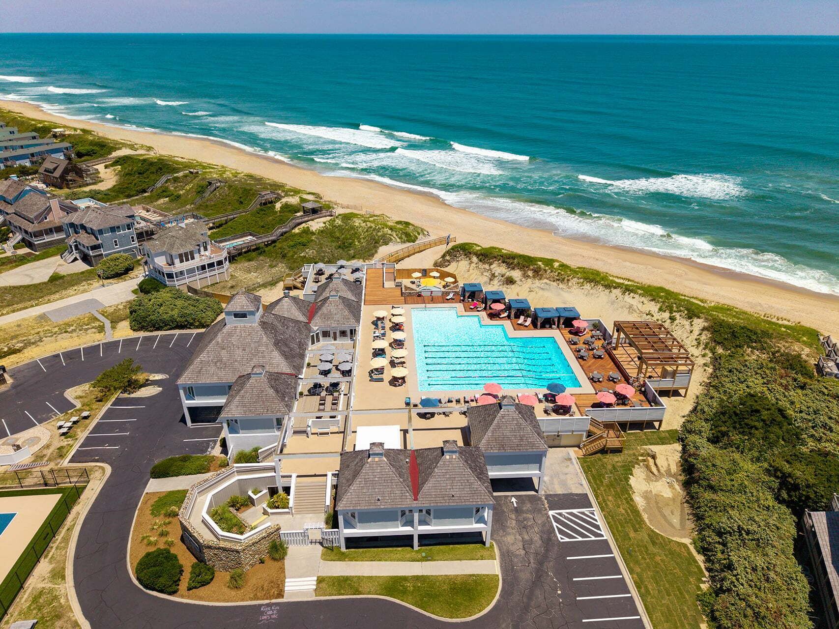 An aerial view of a coastal resort with a swimming pool, beach access, and multiple buildings.