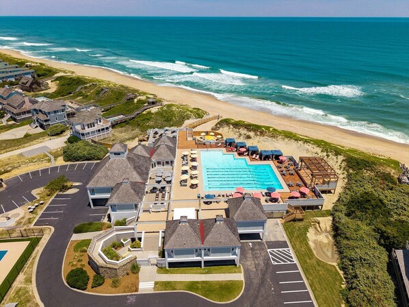 An aerial view of a coastal resort with a swimming pool, beach access, and multiple buildings.