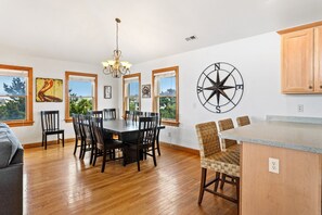 A spacious dining area with a wooden table and chairs, a chandelier, and a large compass wall decoration.
