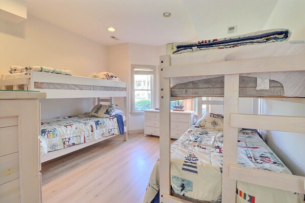 A room with two bunk beds, wooden flooring, a window with blinds, and a radiator. - Wave Rider: Pool, Hot Tub, 5-Min Walk to Beach (Corolla)