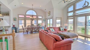 Amplia sala de estar con un sofá rojo grande, comedor con sillas de madera y ventanas grandes que ofrecen una vista.