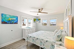 A bedroom with a bed, a dresser, a ceiling fan, and artwork on the walls. - 6BR Beach Walk 3 Min! Pool, Hot Tub & Family Fun (Kill Devil Hills)