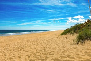 A sandy beach with a wooden fence and vegetation on the right. - 5209 Paradise Found * Ocean Views*Pool (Kill Devil Hills)