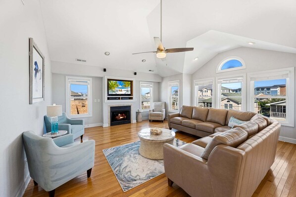 A spacious living room with a fireplace, a large sofa, a television, and a ceiling fan.