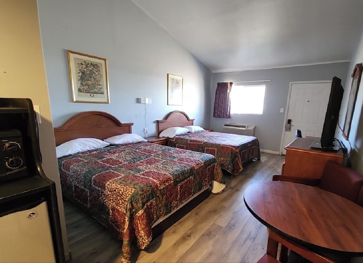 Een kamer met twee bedden, een houten tafel, een televisie en een raam met gordijnen.