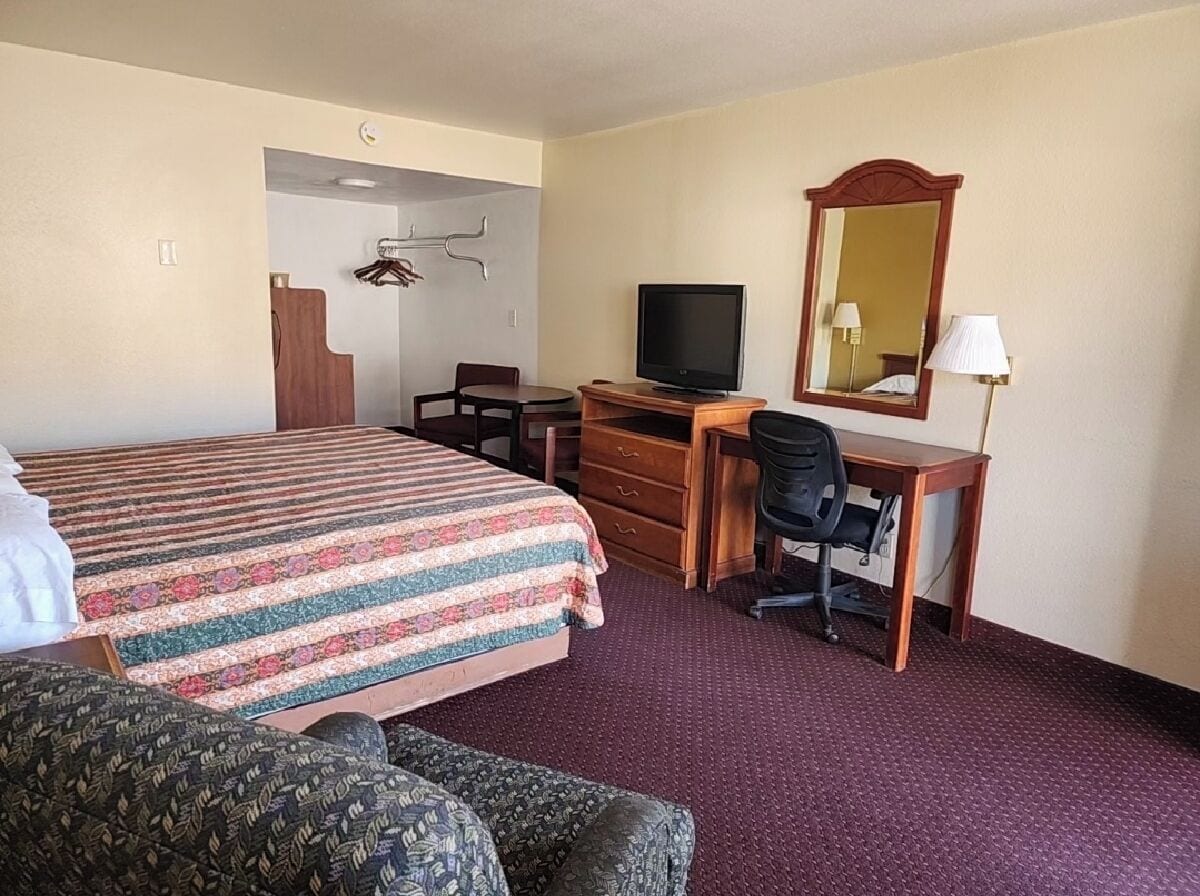 A hotel room with a bed, a desk with a computer, a television, a mirror, and a chair.