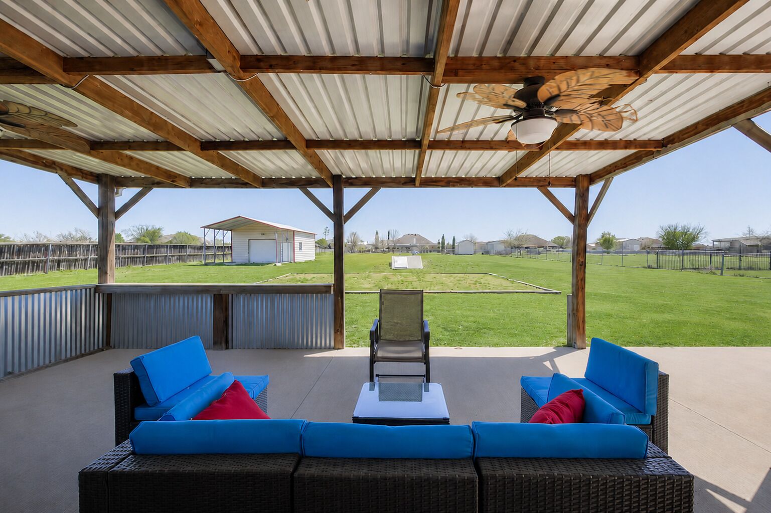 Une terrasse extérieure aménagée avec des meubles en osier et un ventilateur de plafond, donnant sur une pelouse verdoyante.