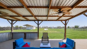 An outdoor patio with wicker furniture and a ceiling fan, overlooking a grassy yard. - Perfect Stay in Ranch-like House with Huge Backyard! (Forney)