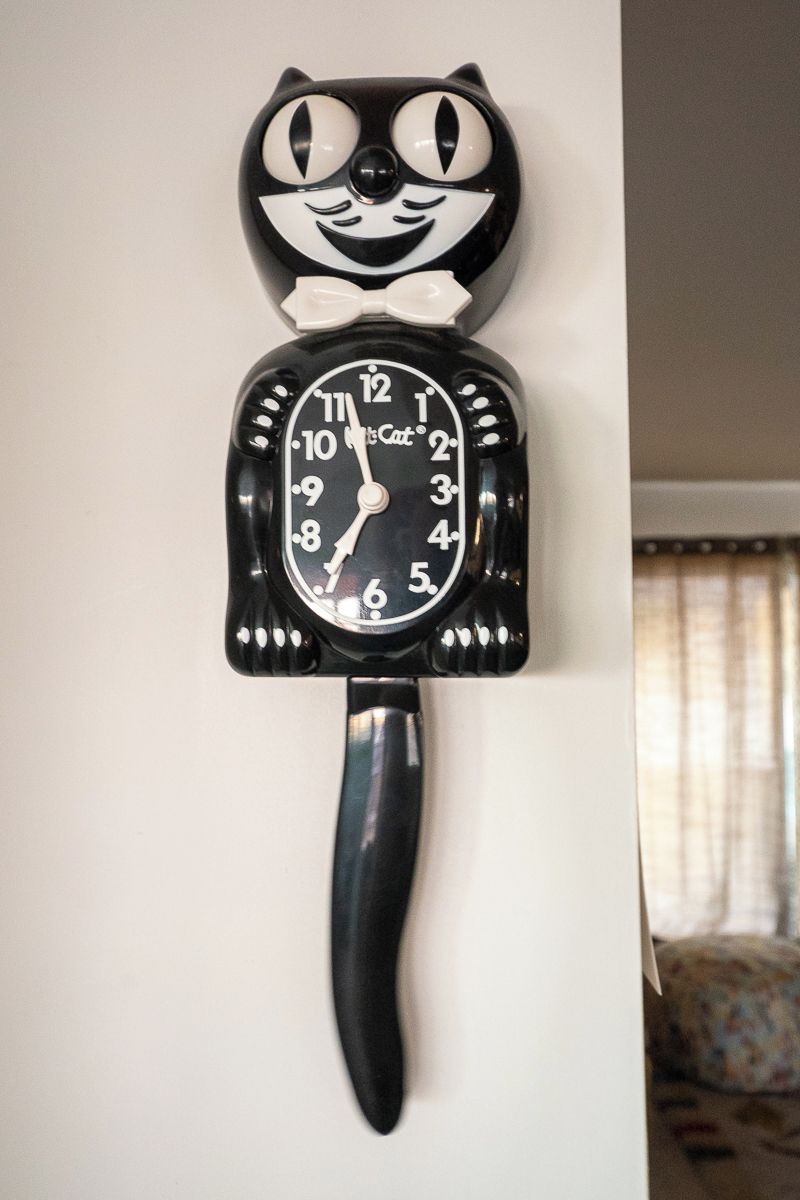 A wall-mounted clock with a cat design, featuring a black and white face and a long black handle.