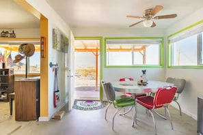 A dining area with a round table, chairs, a ceiling fan, and a view through the windows.