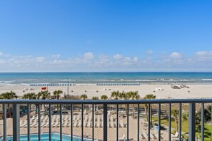 A beach view from a balcony with a pool area, lounge chairs, and umbrellas. - The Summit Unit 512 (Panama City Beach)