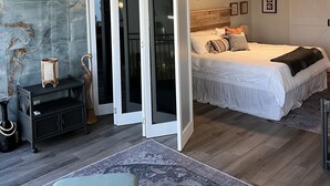A modern bedroom with a large bed, a ceiling fan, and a view through a sliding door to a balcony.