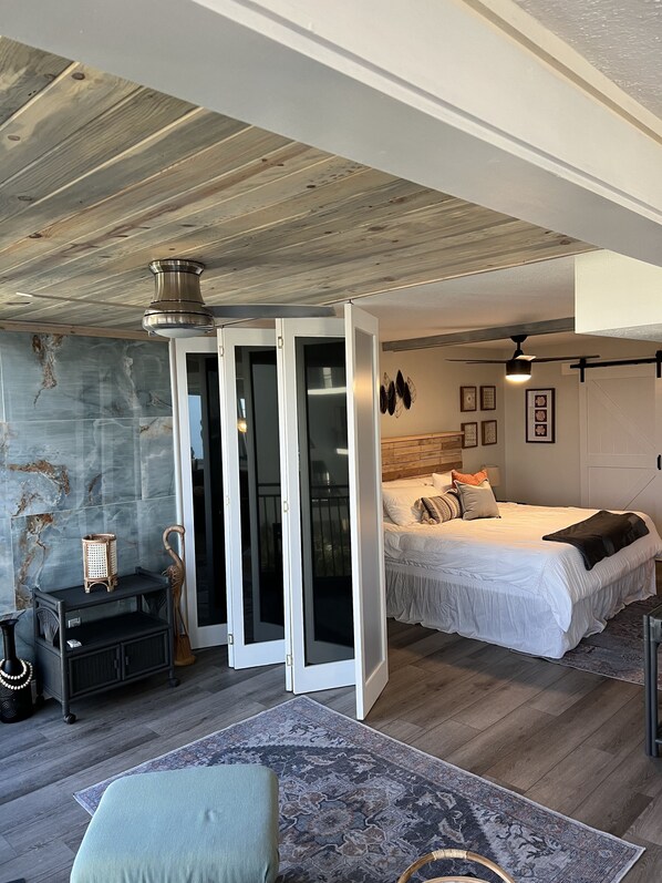 A modern bedroom with a large bed, a ceiling fan, and a view through a sliding door to a balcony.