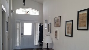 Een gang met een witte deur, een lamp en ingelijste foto's aan de muur.