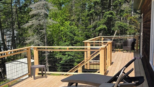 Una terraza de madera con sillones de descanso y una mesa, rodeada de árboles.