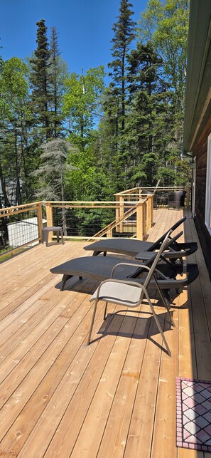Una terraza de madera con sillones de descanso y una mesa, rodeada de árboles.