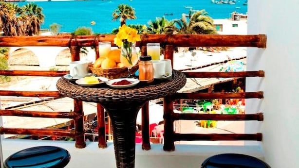A balcony with a table set for breakfast, overlooking a coastal area with boats and buildings.