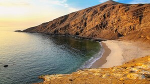 A coastal landscape with a sandy beach and rocky cliffs.