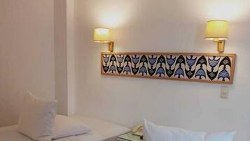 Une chambre d’hôtel avec deux lits simples, chacun doté de draps et d’oreillers blancs. Deux lampes murales sont fixées au mur, au-dessus des lits, et un panneau décoratif se trouve également au-dessus.