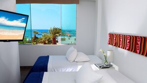 A hotel room with a bed, a TV, a window with a view of the sea, and a wall with a striped pattern.