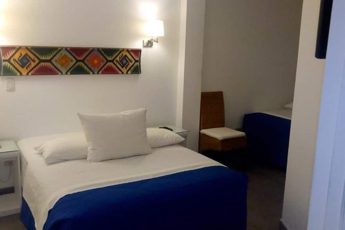 Ein Hotelzimmer mit einem Bett, einem Sessel, einem Nachttisch mit Telefon und einer Wandleuchte.