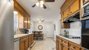 Une cuisine avec des meubles de rangement en bois, un réfrigérateur, une cuisinière et un ventilateur de plafond.