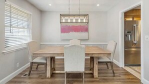 Une salle à manger avec une table en bois et quatre chaises, un luminaire suspendu et un grand tableau abstrait accroché au mur.