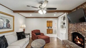 Un salon doté d’une cheminée, d’un ventilateur de plafond et d’un téléviseur fixé au mur.