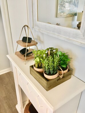 A white console table with a wooden plant stand holding three black speakers and a wooden tray with potted plants.
