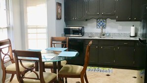 Une cuisine avec des meubles de rangement de couleur sombre, un four à micro-ondes et une table à manger avec des chaises.