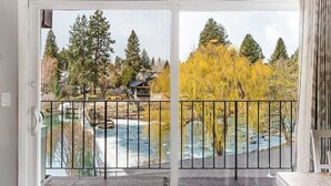 A view through a glass door of a river with trees and a house in the background.