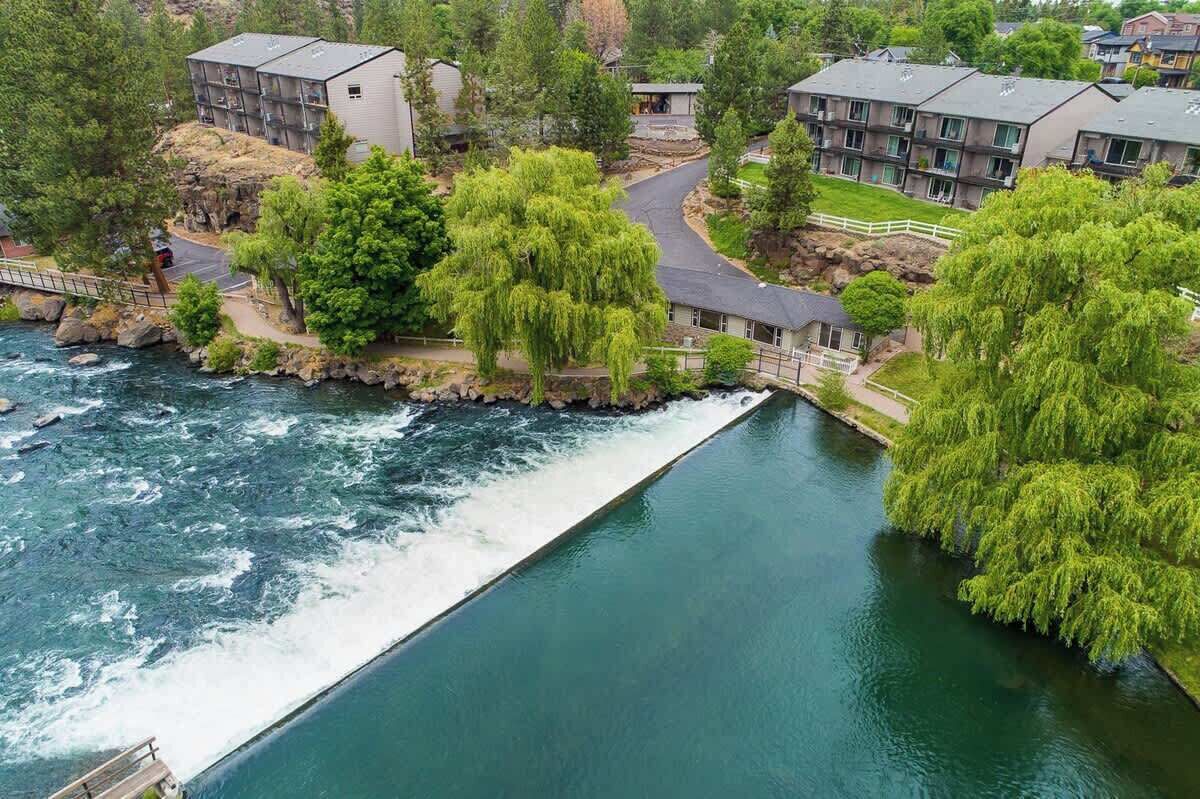 A river flowing through a residential area with modern buildings, a bridge, and lush greenery.