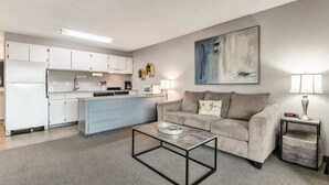 A modern living room with a sofa, coffee table, and a kitchen area in the background.