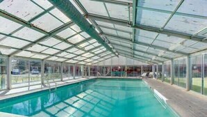 An indoor swimming pool with a glass ceiling, surrounded by a wooden deck.
