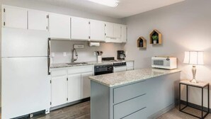 A modern kitchen with white cabinets, a granite countertop, a built-in microwave, and a small side table with a lamp.