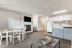 Uma sala de estar moderna com lareira, área de jantar e cozinha com armários brancos e uma TV de tela plana.
