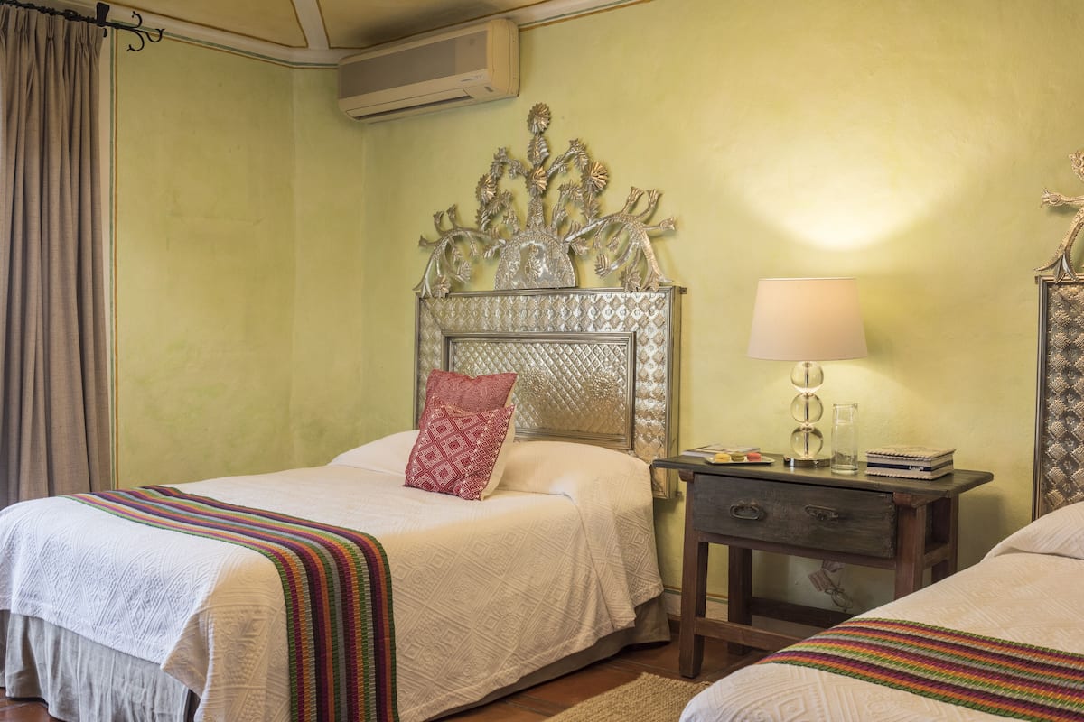 A bedroom with two beds, a decorative headboard, a bedside table with a lamp, and a small nightstand.
